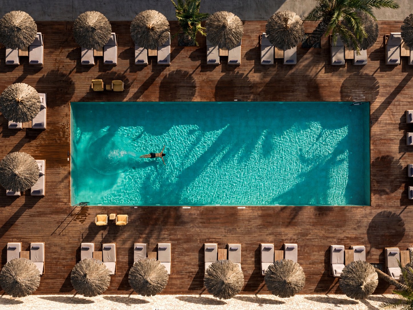 A turquoise resort pool with sun loungers and shaded parasols